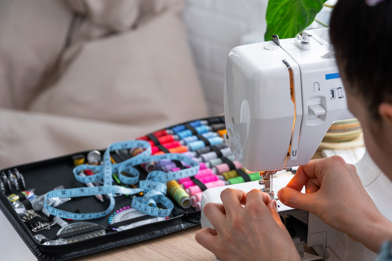 Femme qui enfile une aiguille sur sa machine à coudre avec accessoires et fils en arrière-plan.