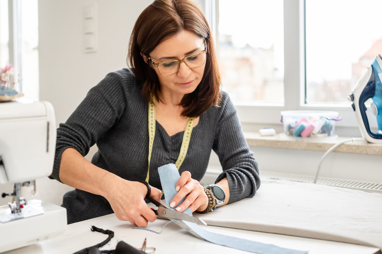 Couturière qui coupe un tissu couleur denim à l’aide d’un ciseau de couture, dans son atelier.