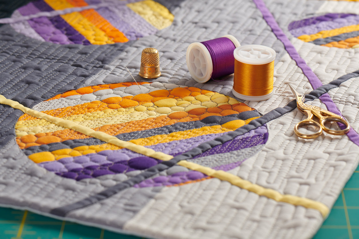 Accessoires de couture sur une courtepointe dans les teintes dorées et mauves.