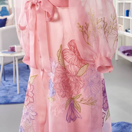 Bernina 990 machine à coudre permettant la broderie fine sur un vêtement rose transparent, ajoutant des motifs floraux délicats.