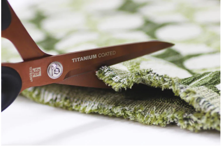Gros plan des ciseaux TITECH Pro coupant un tissu épais, montrant leurs lames en titane et leur précision de coupe.