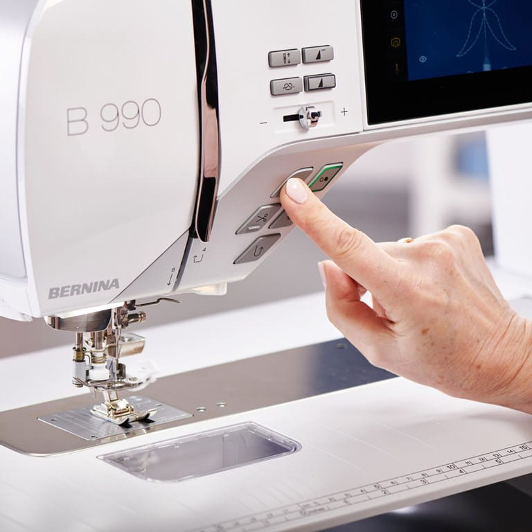 Gros plan sur le panneau de commandes Bernina 990 machine à coudre – Une main appuyant sur un bouton pour activer la machine, près du pied-de-biche.