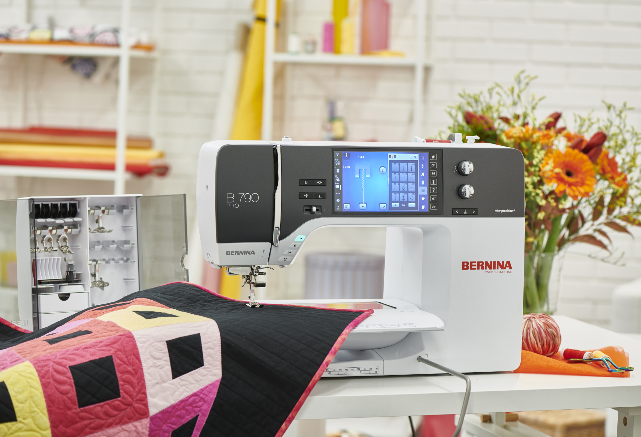 Machine à coudre Bernina B 790 PRO avec un quilt coloré – Machine à coudre réalisant des surpiqûres sur un quilt aux motifs géométriques, avec des accessoires de couture visibles en arrière-plan.