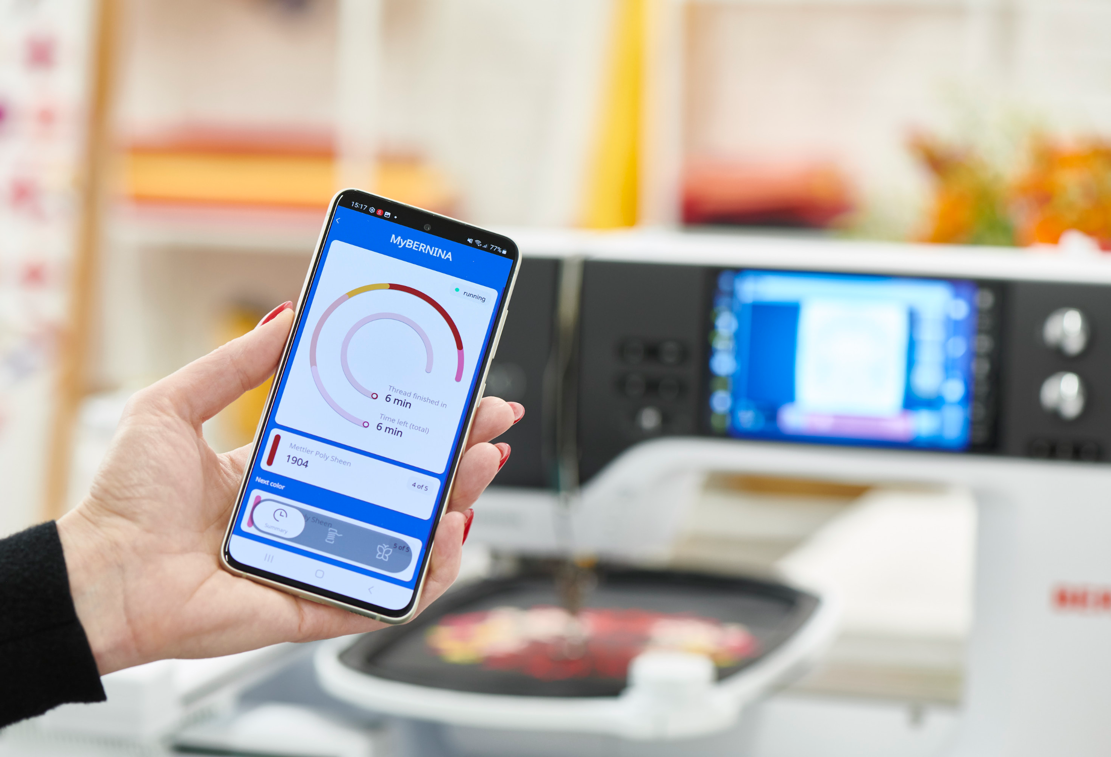 Machine à coudre Bernina B 790 PRO connectée à une application mobile – Gros plan sur une main tenant un smartphone affichant l’application MyBernina, permettant de suivre l’avancement du projet de broderie à distance.