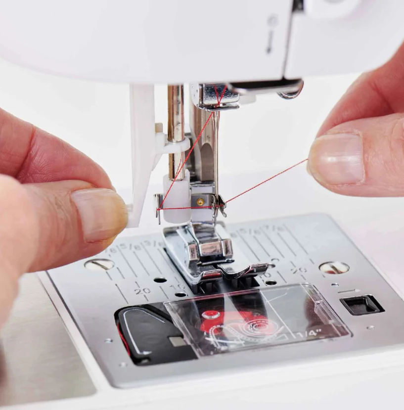 Machine à coudre SINGER CE677 Elite – Gros plan sur l’enfilage automatique de l’aiguille, démontrant le passage du fil rouge dans le mécanisme.