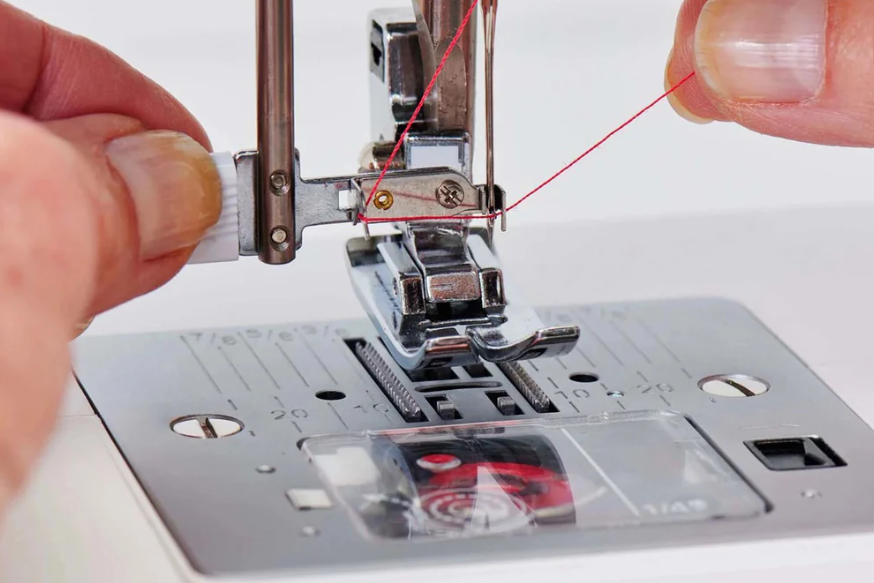 Machine à coudre SINGER Elite ME457 – Gros plan du système d’enfilage automatique de l’aiguille, avec une démonstration de l’enfilage du fil rouge.