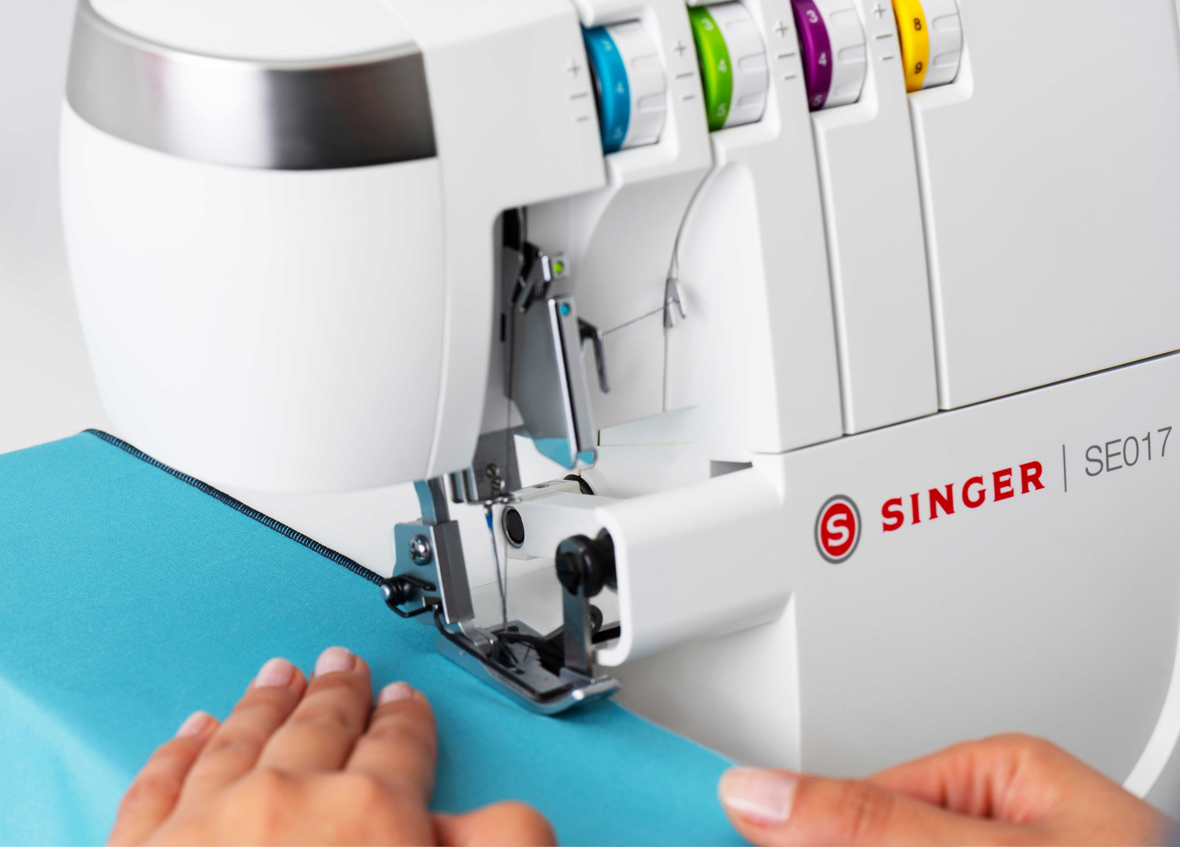 Machine à coudre surjeteuse SINGER Elite SE017 – Surjeteuse en action avec un tissu bleu, montrant une couture nette et résistante.
