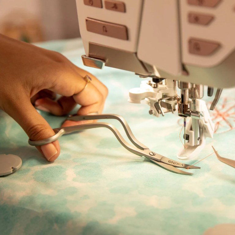 Main utilisant les ciseaux de broderie à double courbure Husqvarna Viking pour couper des fils autour d’un cadre de broderie.