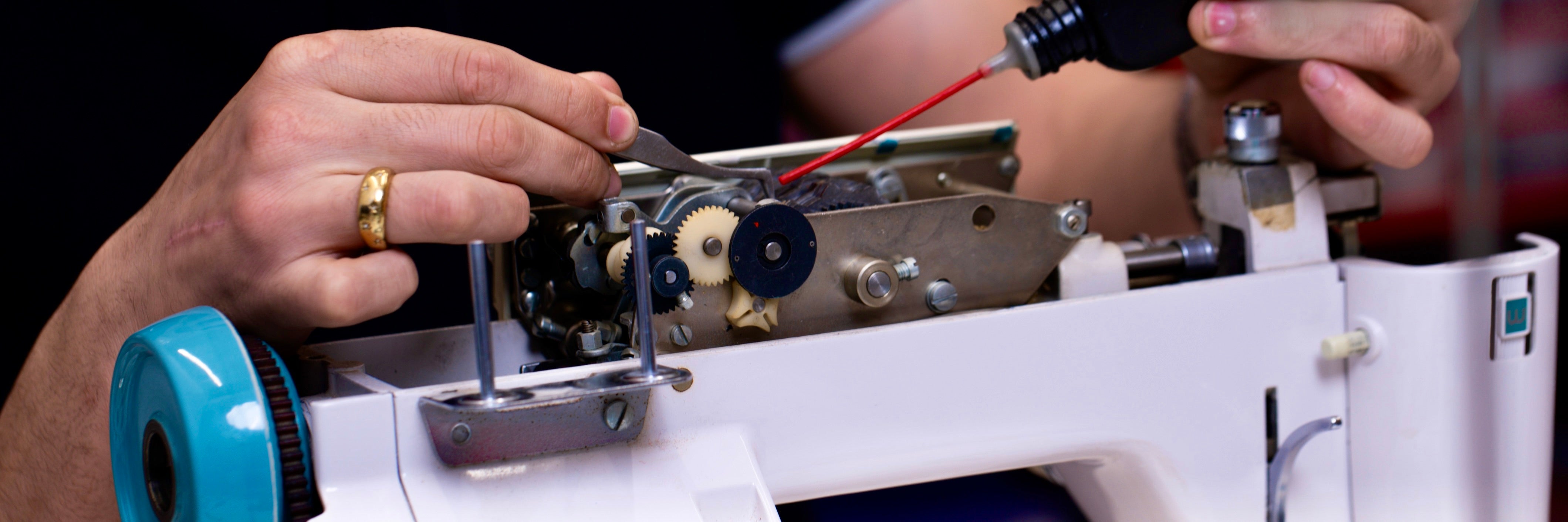 Gros plan sur les mains d'une technicienne qui utilise des outils pour réparer les engrenages d'une machine à coudre