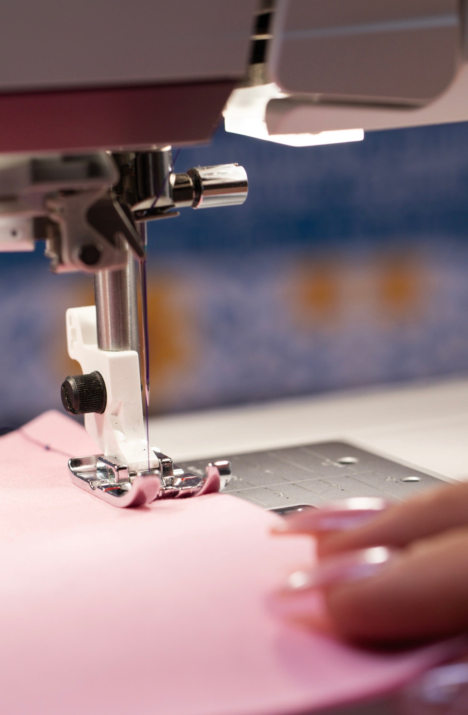 Gros plan sur les mains d'une couturière et sur l'aiguille de la machine, en train de coudre un tissu rose