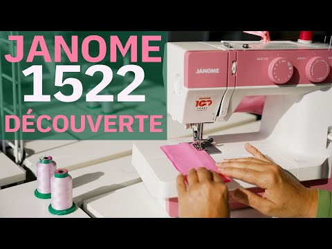 Machine à coudre mécanique Janome 1522 en édition rose, en train de coudre un tissu rose, avec des bobines de fil à l'avant-plan et un texte 'Janome 1522 Découverte' affiché à l'écran.