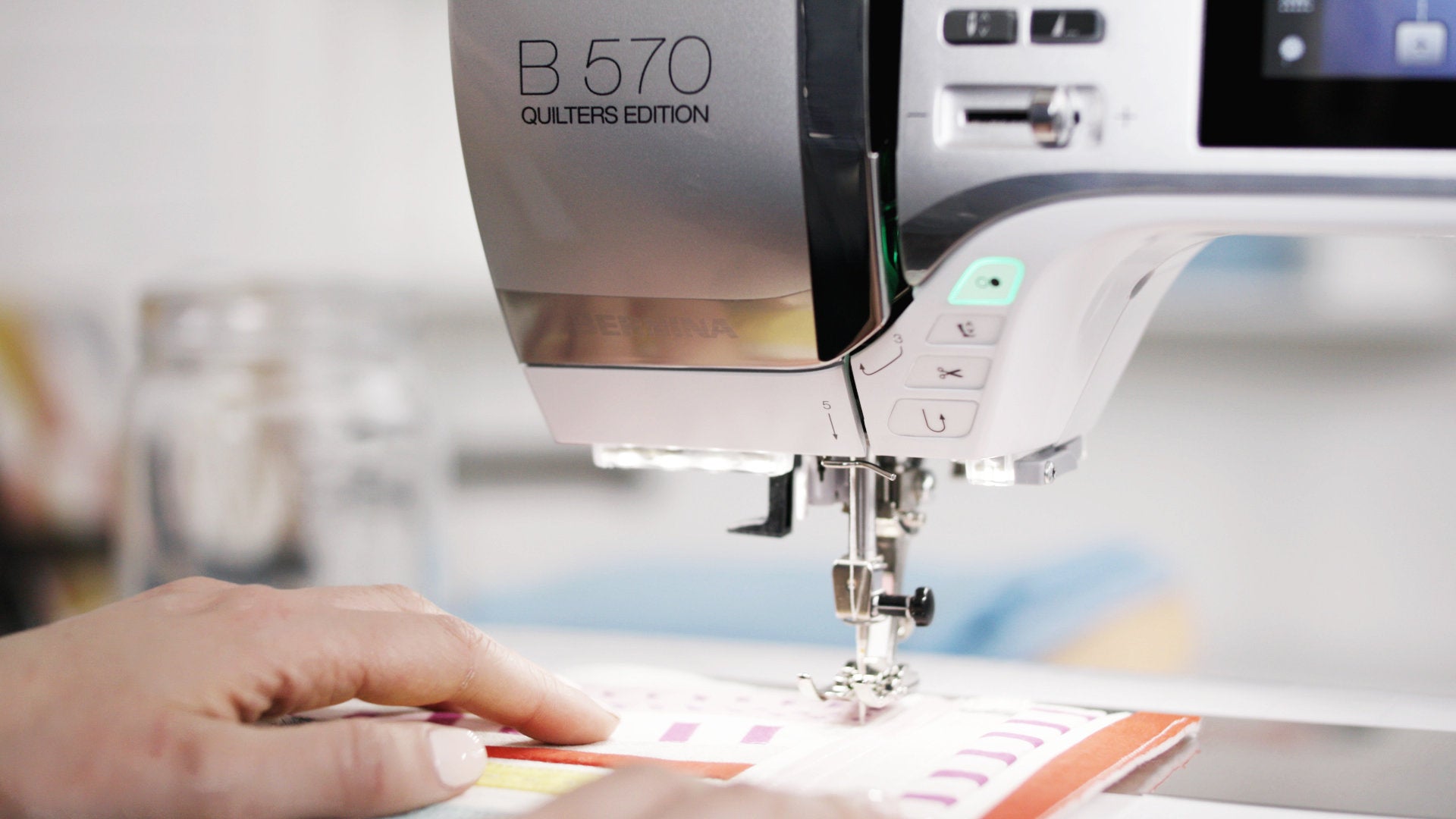 Machine à coudre Bernina 570 QE en action – Gros plan sur la machine en train de coudre un projet textile coloré, avec des commandes intuitives et un éclairage LED.