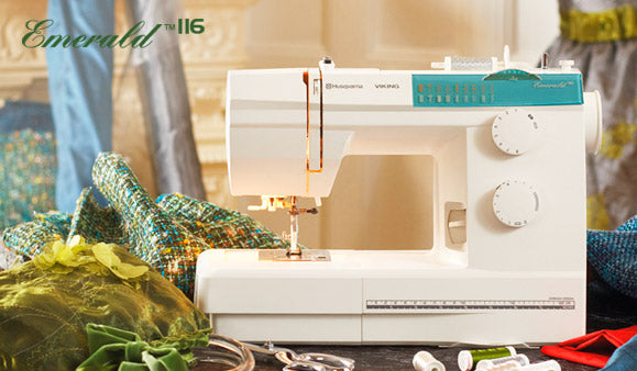 Machine à coudre Husqvarna Viking EMERALD™ 116 en atelier de couture – Présentation de la machine dans un environnement créatif avec tissus, fils et accessoires, idéale pour la couture domestique et les projets de confection.