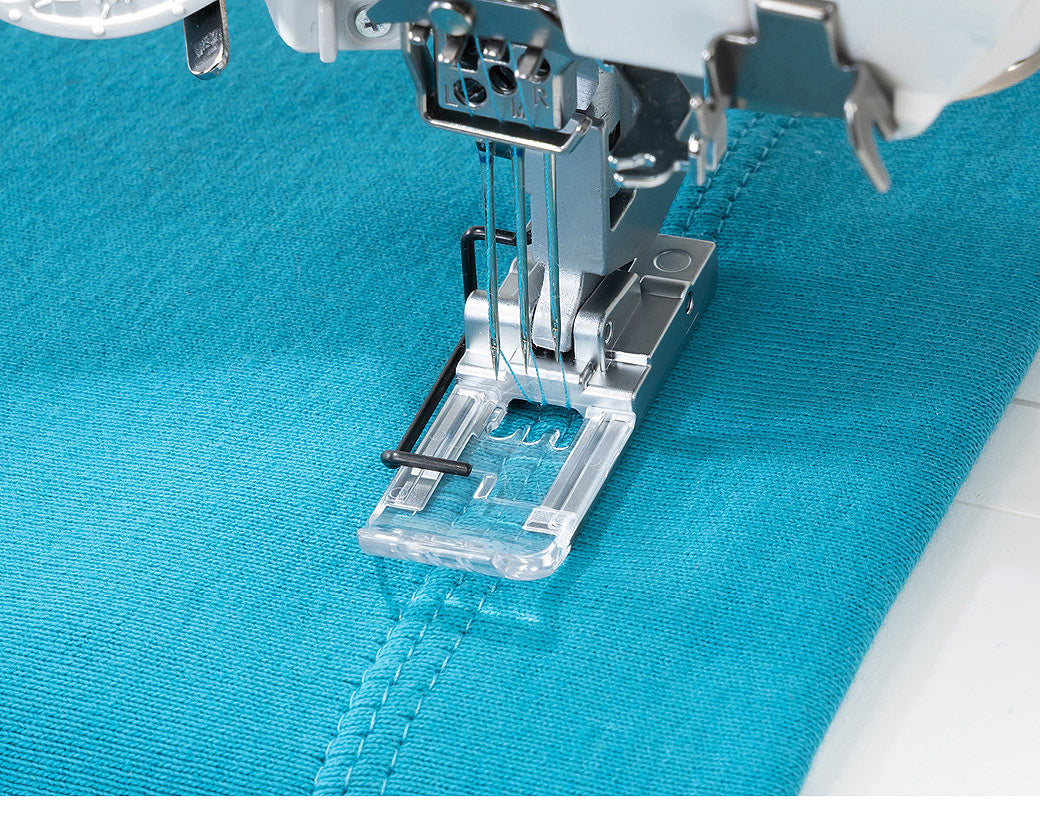 Machine à coudre recouvreuse Janome CoverPro 3000 Professional – Gros plan du pied-de-biche cousant une double couture sur un tissu bleu, démontrant la finition précise et professionnelle.