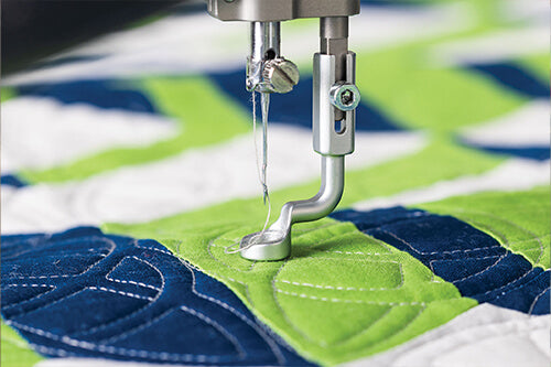 Machine à quilter Grace Q'nique 19X Elite en gros plan sur l’aiguille et le pied de biche, réalisant des coutures détaillées sur un quilt vert et bleu.
