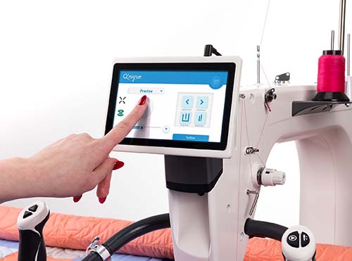 Machine à quilter Q'nique 21X Elite avec écran tactile, affichant une interface de contrôle intuitive pour ajuster les paramètres de couture, avec une main sélectionnant une option.