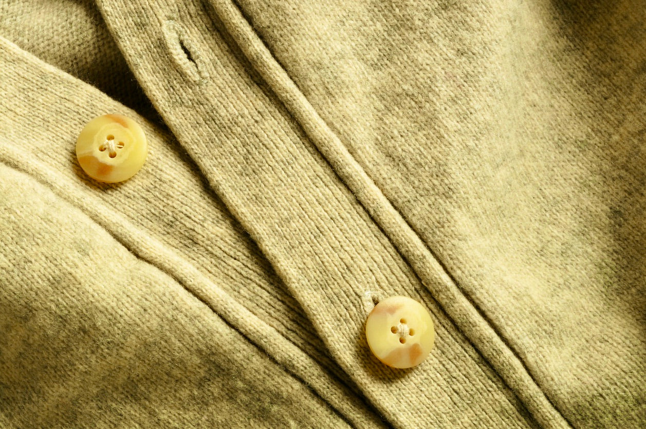 Gros plan sur les boutons et la boutonnière d'un cardigan beige doré