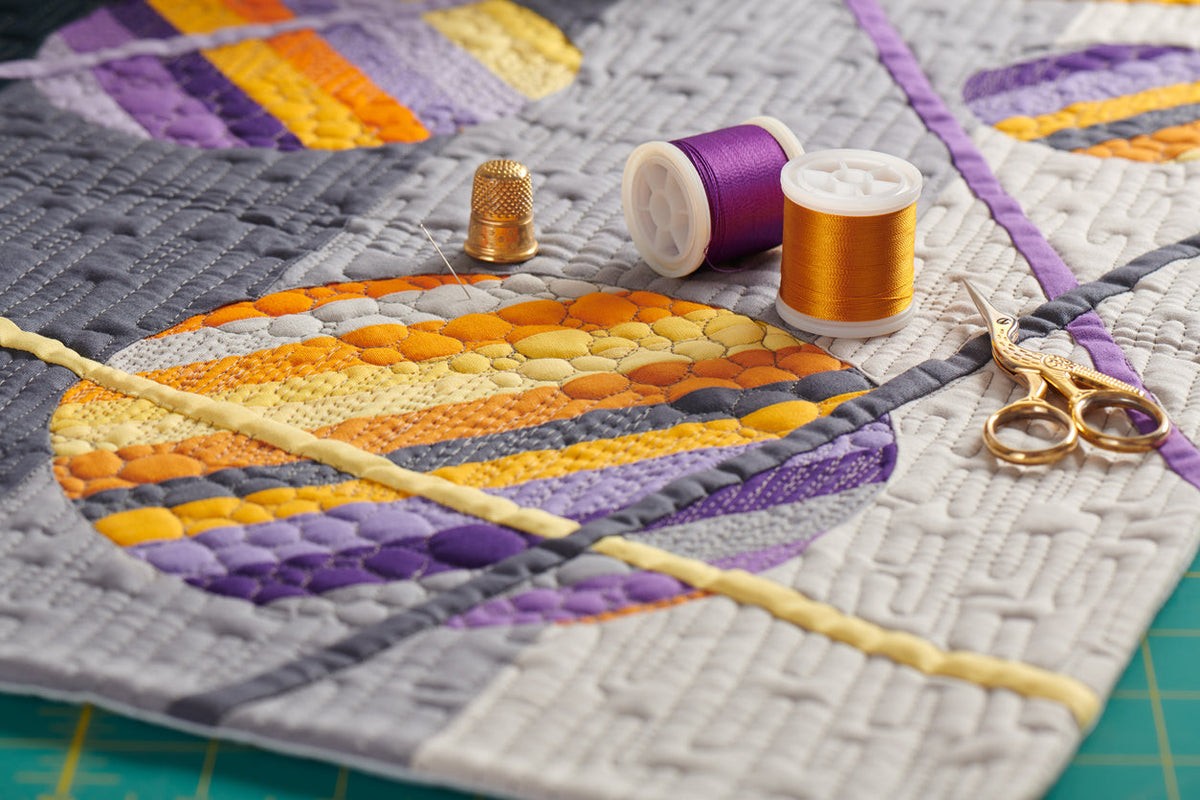 Accessoires de couture sur une courtepointe dans les teintes dorées et mauves.