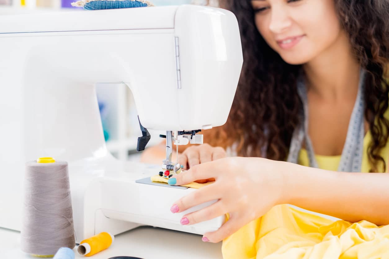 Jeune femme qui sourit en utilisant une machine à coudre pour débutant.