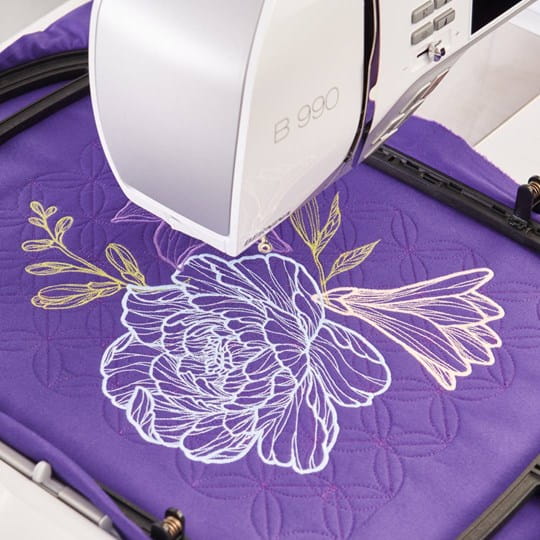 Bernina 990 machine à coudre en pleine broderie d'un motif floral détaillé avec fils colorés sur un tissu violet.