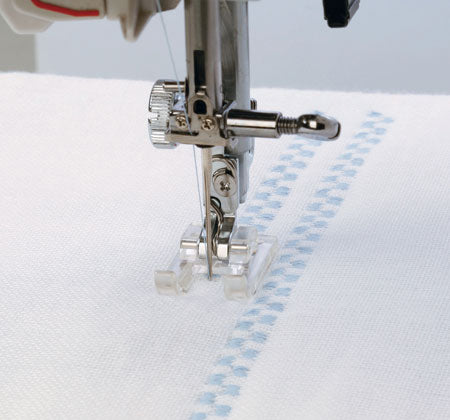 Machine à coudre Janome MyStyle 100 en pleine couture, réalisant un point décoratif précis sur un tissu blanc.
