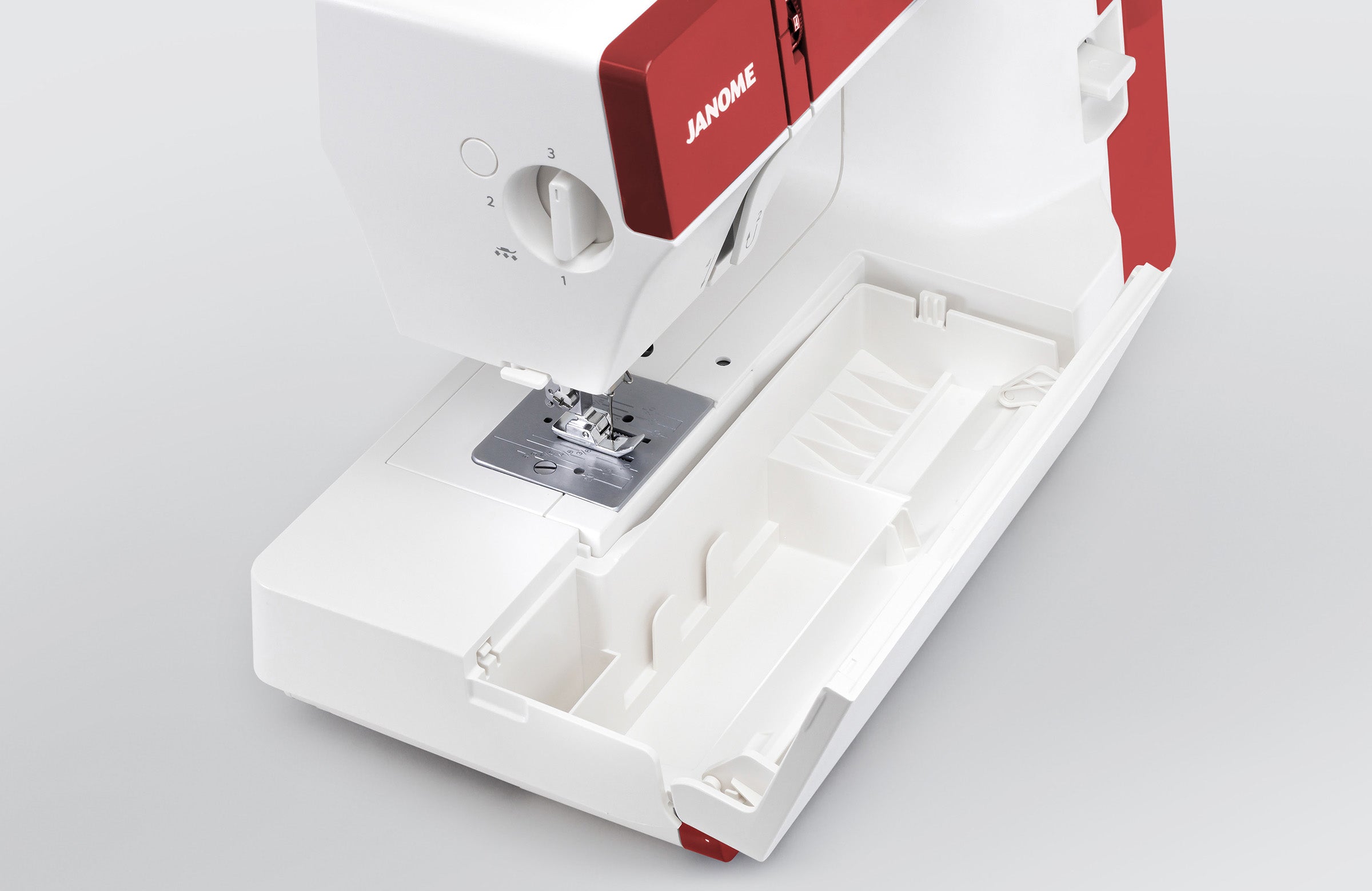 Machine à coudre mécanique Janome 1522RD avec le compartiment de rangement ouvert, offrant un espace pour accessoires sous la machine.