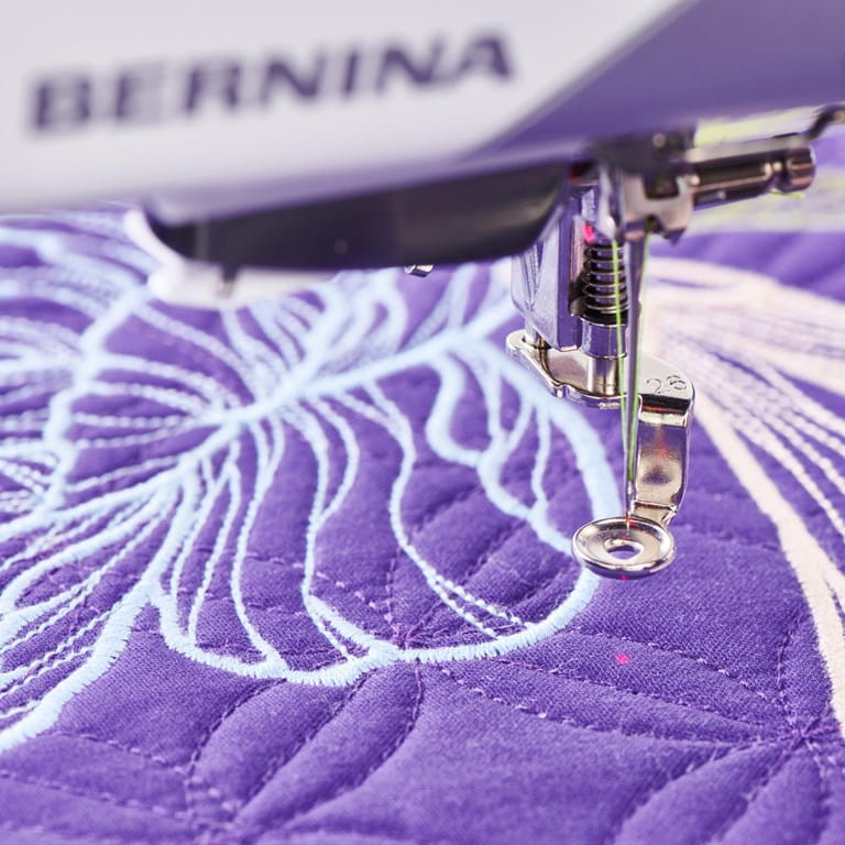 Pied-de-biche Bernina 990 machine à coudre en broderie – Aiguille et pied presseur cousant un motif floral sur un tissu violet.