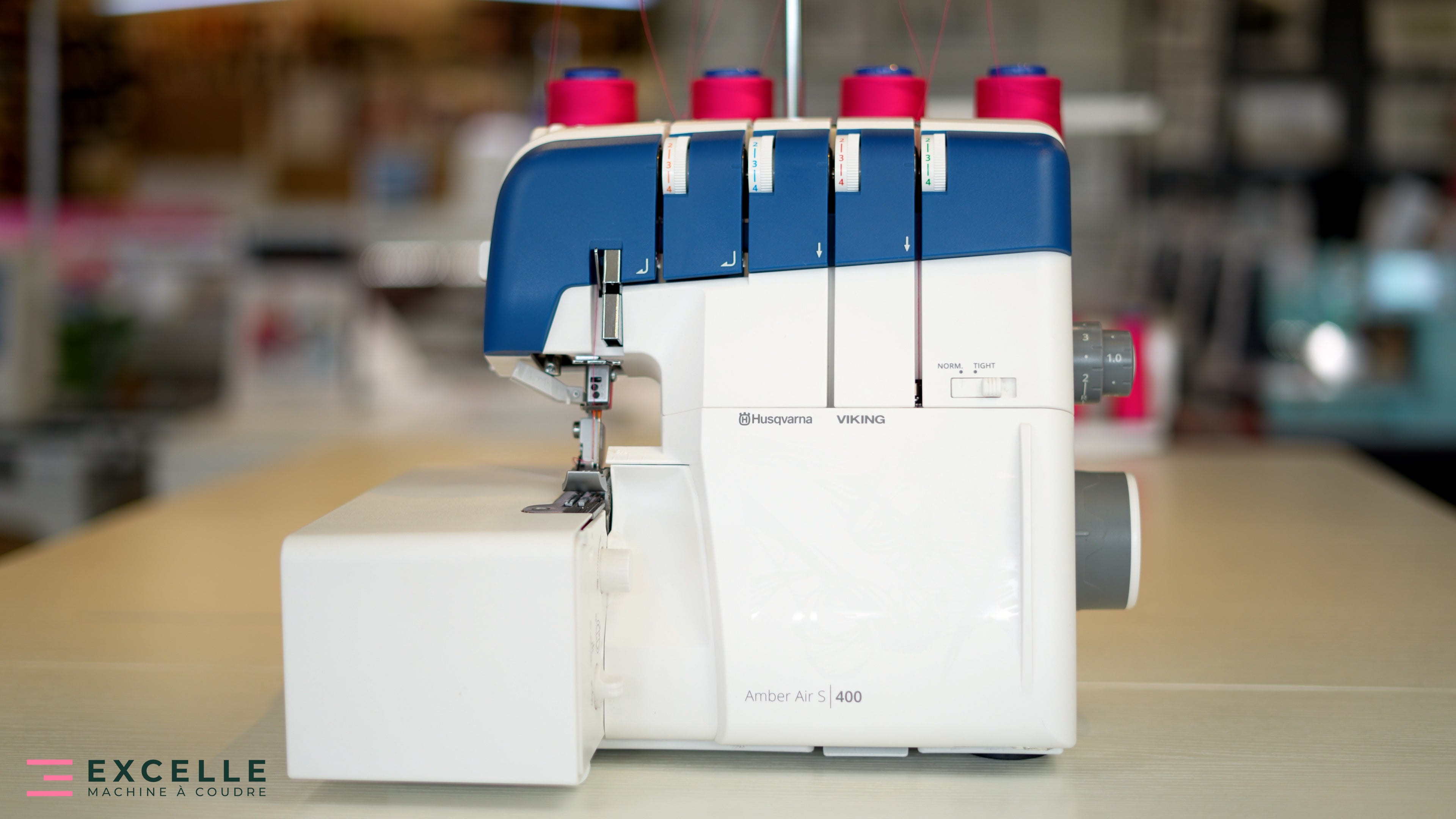 Surjeteuse Husqvarna Viking AMBER™ Air S | 400 en boutique – Vue détaillée de la machine installée sur une table, équipée de fils rose vif, illustrant son design ergonomique et moderne.