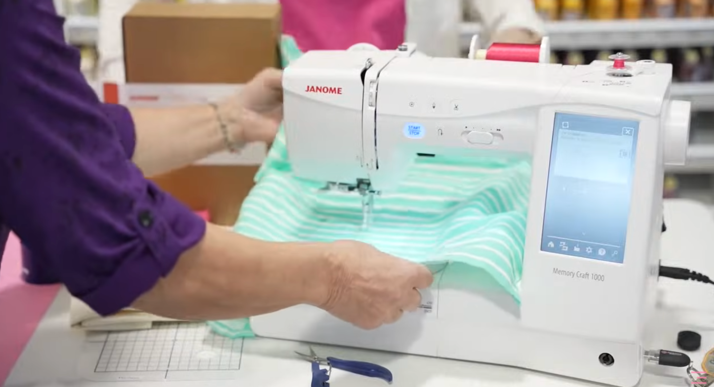 Conseillère chez Excelle Machine à Coudre qui tient un tissu vert menthe en présentant une machine à broder Janome