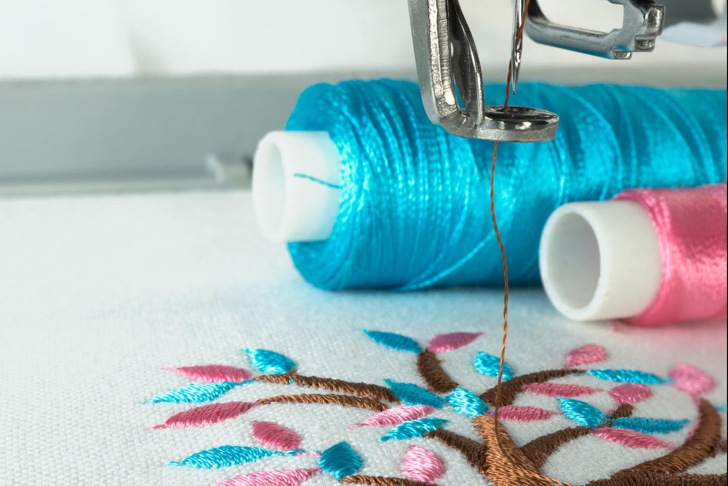 Gros plan sur une création à la broderie machine, avec des bobines de fils bleus et roses en arrière-plan
