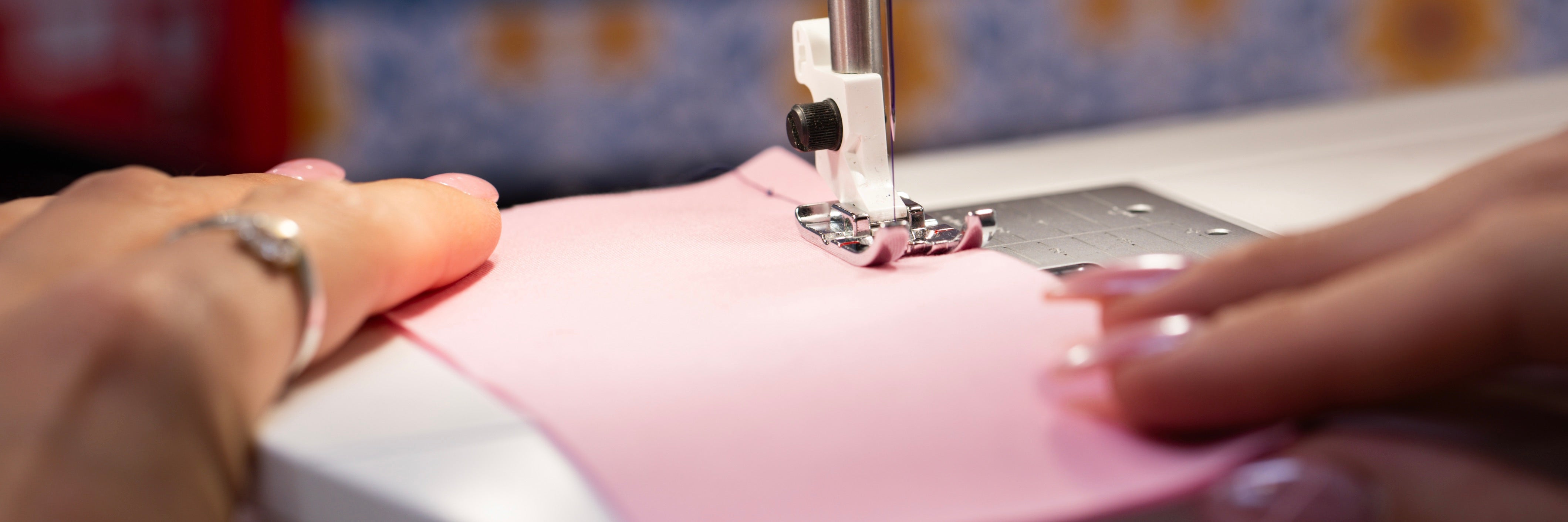 Gros plan sur les mains d'une couturière qui est en train de coudre un tissu rouge à la machine