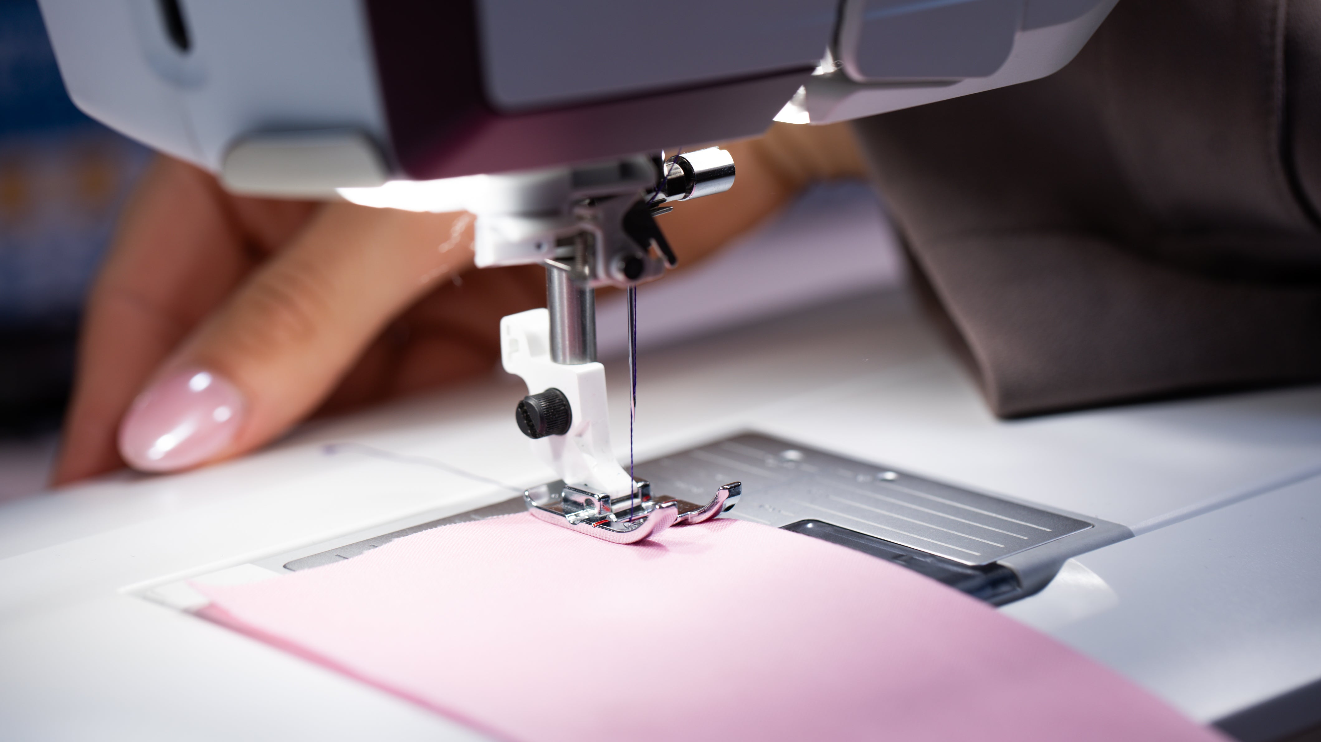 Gros plan sur l'aiguille d'une machine à coudre travaillant sur un tissu rose