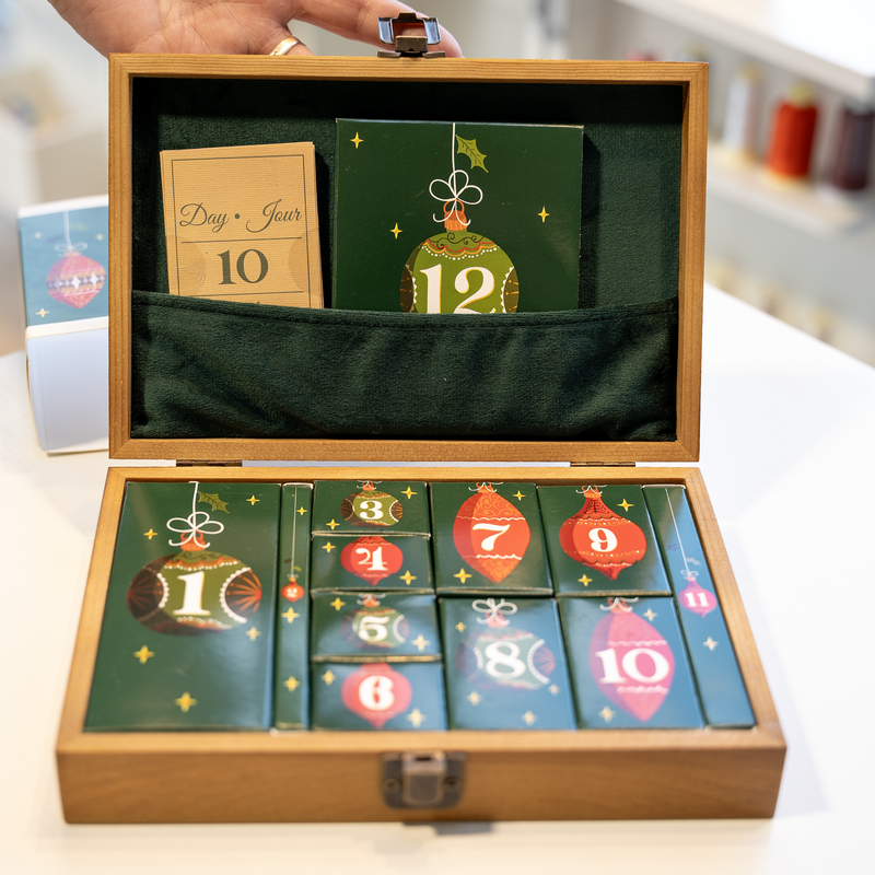 Coffret ouvert du calendrier de l’Avent couture '12 jours de Noël en piqûres', révélant des enveloppes surprises numérotées de 1 à 12.