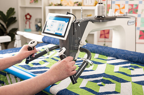 Machine à quilter Grace Q'nique 19X Elite avec un écran tactile interactif, affichant les réglages de couture, utilisée par un couturier pour un quilting précis sur un tissu coloré.