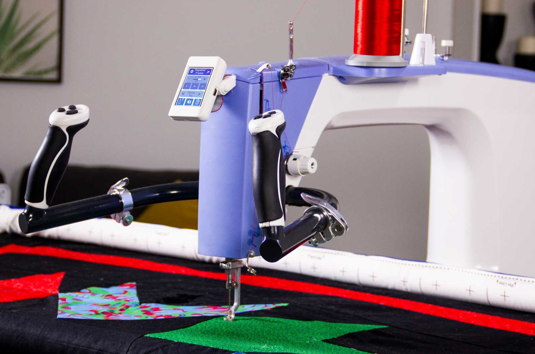 Machine à quilter Q'nique 19 en action, piquant un quilt coloré avec un fil rouge, dotée d'un écran numérique tactile et de poignées ergonomiques pour un contrôle précis.