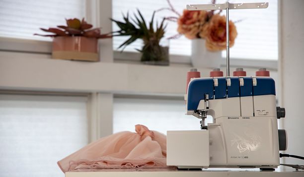 Surjeteuse Husqvarna Viking AMBER™ Air S | 400 dans un atelier de couture – Machine positionnée sur une table avec un tissu en mousseline rose, soulignant son adaptabilité pour des tissus délicats.