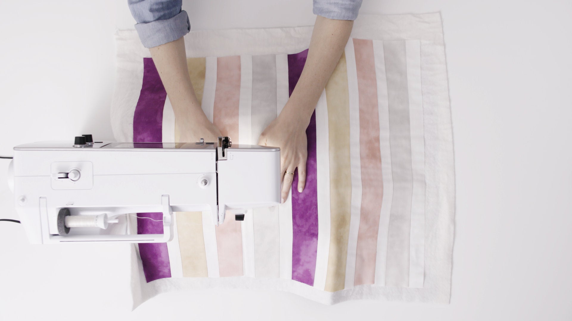 Vue de dessus d’une machine à coudre Bernina 570 QE – Couture d’un quilt à rayures pastel avec une machine à bras libre, offrant une grande précision et un espace de travail généreux.